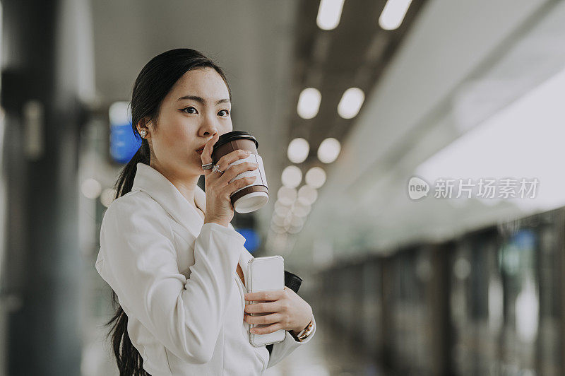 一位年轻的亚洲华裔女商人在单轨火车站边等车边喝咖啡