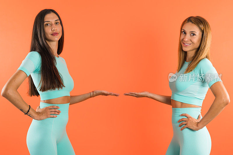 运动女孩在同样的运动服装展示一个产品，伸出的手在中间。复制空间工作室拍摄