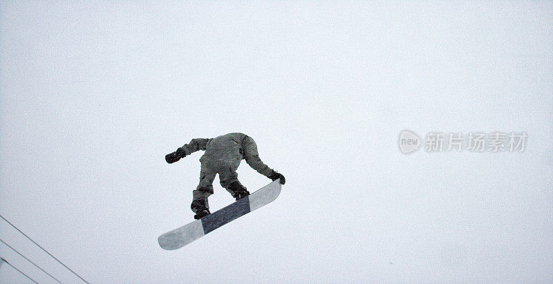 一个滑雪板在完整的冬季装备试图在一个“背面360”伎俩在博尔德附近的埃尔多拉滑雪度假村，科罗拉多州在一个下雪，阴天