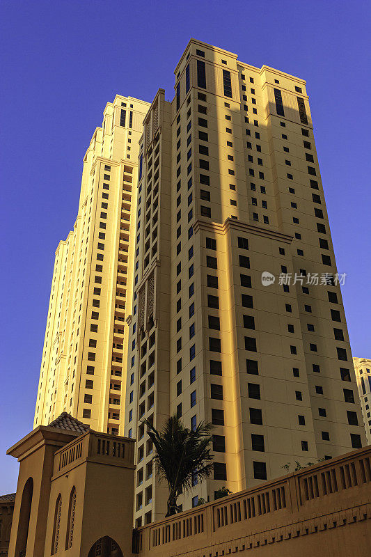 阿拉伯联合酋长国迪拜——仰望城市中朱美拉海滩住宅的一些塔的顶端，在晴朗的蓝色夜空下;垂直格式