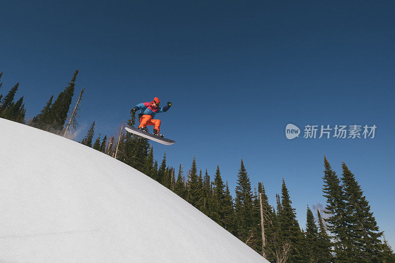 滑雪板男子跳过雪上滑雪斜坡。晴朗的一天，在滑雪胜地，美丽的山景观