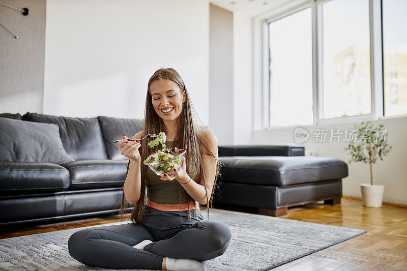 一个年轻女子在她的客厅里吃新鲜的蔬菜沙拉