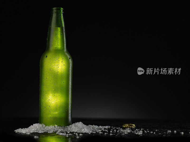 冰冷的绿色啤酒瓶上覆盖着水滴-凝结。空白饮料饮料产品设计模型。站在黑色的桌子上，黑色的背景。