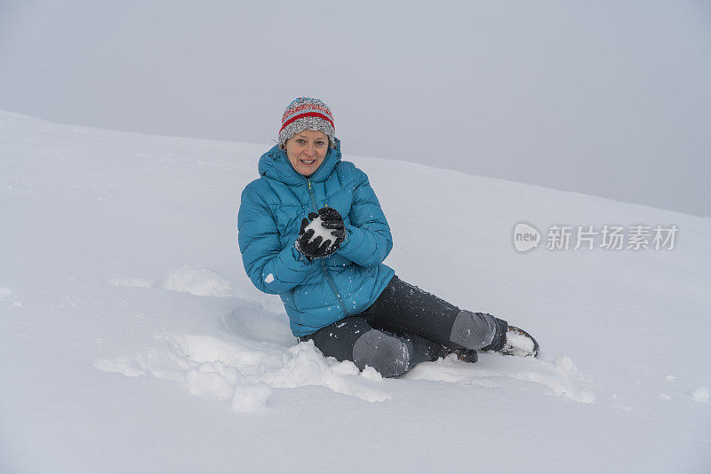 成熟的女人穿着皮大衣在雪地里扔雪球