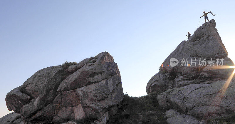 远处两名攀登者登上岩壁顶峰，日出的景象