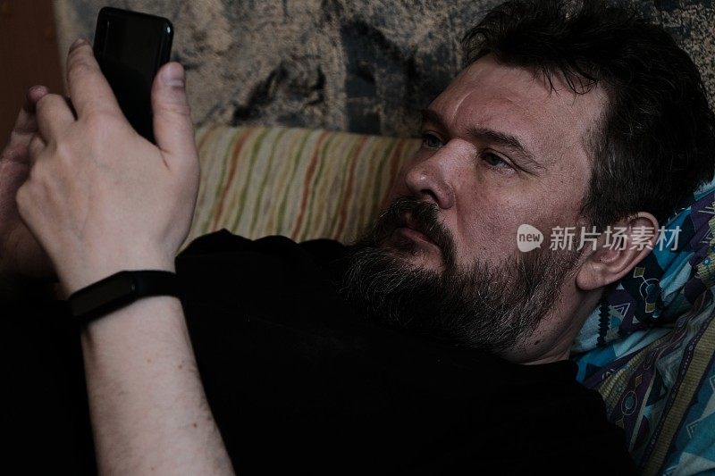 特写照片的成熟男子躺在沙发上，使用他的智能手机