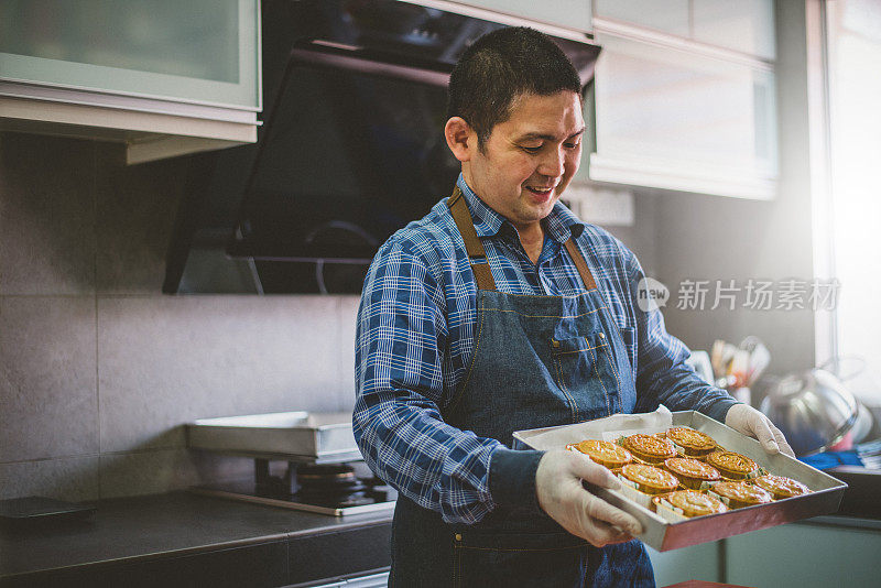 一名亚洲男子从烤箱烤好月饼后，拿着自制的月饼放在烤盘上