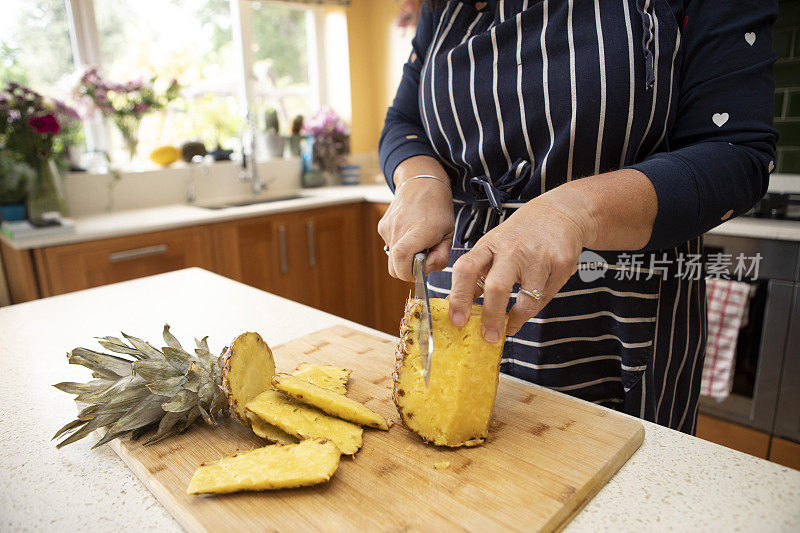 一个女人站在厨房里用刀切菠萝皮
