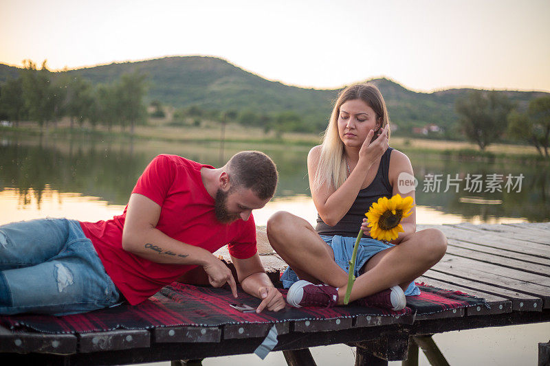 一对年轻夫妇坐在湖边码头上欣赏日落