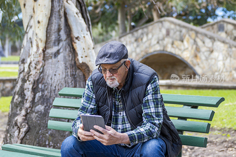一位老人独自坐在公园里使用迷你数码平板电脑
