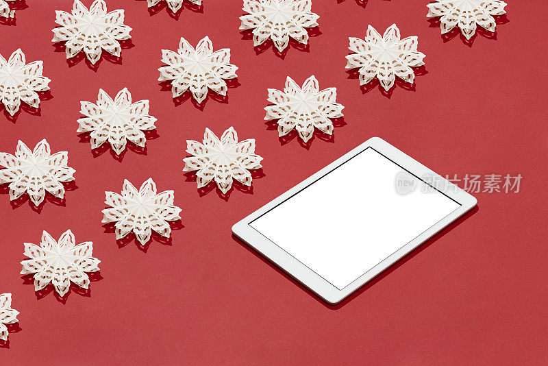 数字平板电脑模型与白色雪花圣诞装饰平放在红色背景