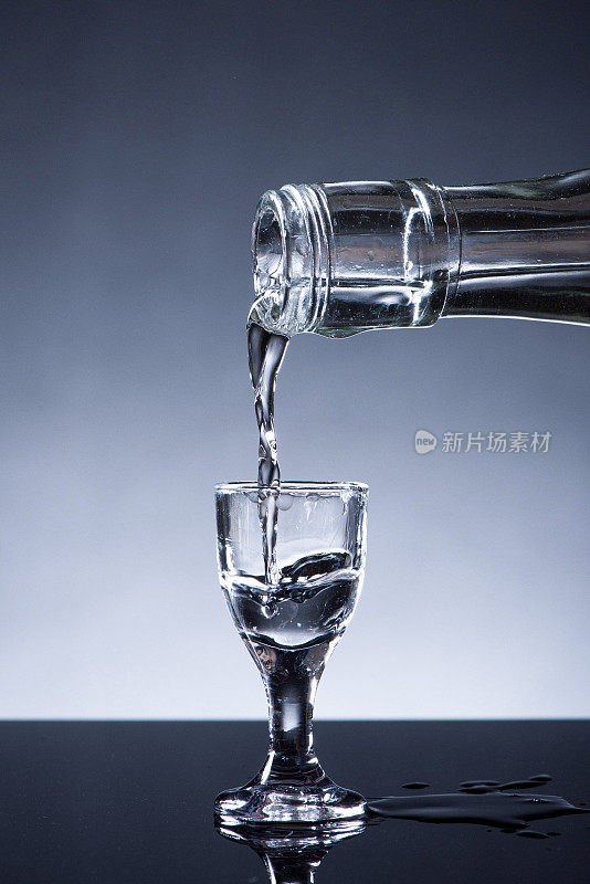 白酒或烈酒是从一个瓶子背景倒进一个玻璃杯