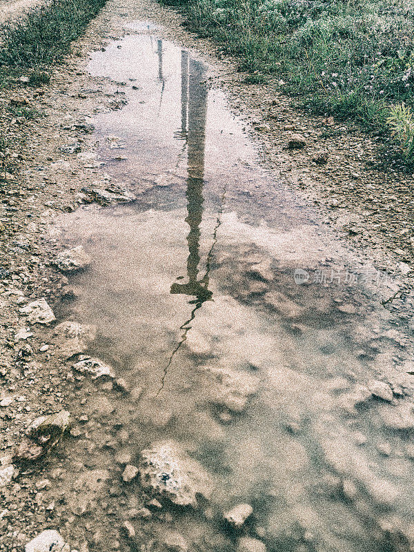 风力涡轮机在转动，反射在雨后泥泞道路上的水坑里。绿色能源来自风力发电机。