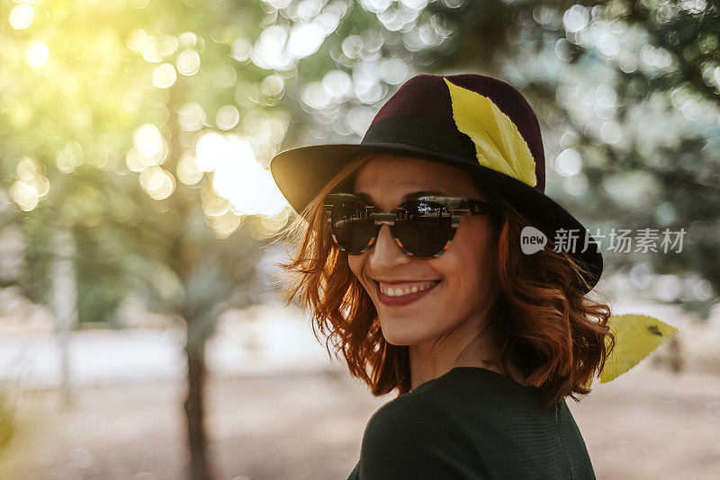 一个戴着帽子和太阳镜的女人的肖像，在秋天微笑着感到幸福。