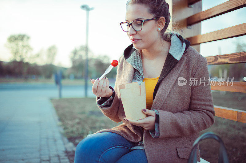 这个女人坐在公园的长椅上，吃着纸箱里的食物。