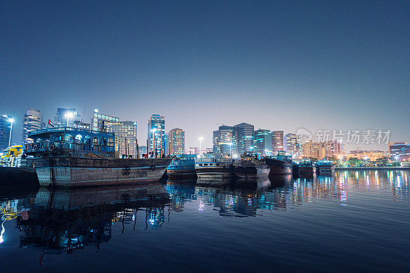 传统的阿拉伯船只停泊在迪拜河，后面是现代建筑