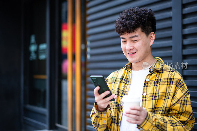 亚洲年轻英俊男子在城市街道上使用智能手机