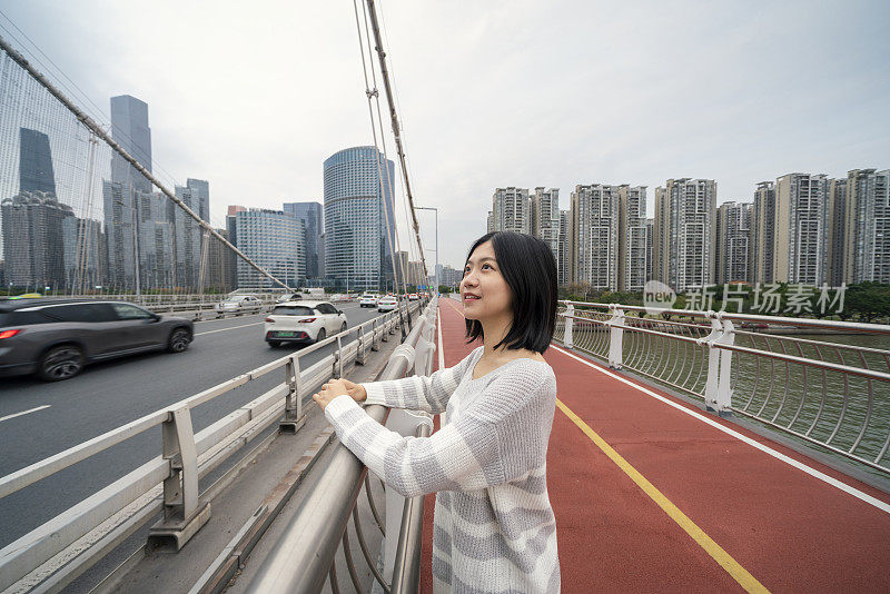 在市中心的一座桥上，一位亚洲妇女望着远方