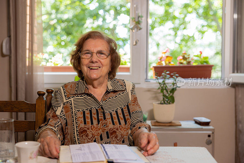 开朗的老年高加索妇女的肖像，94岁，坐在桌子和阅读一本书