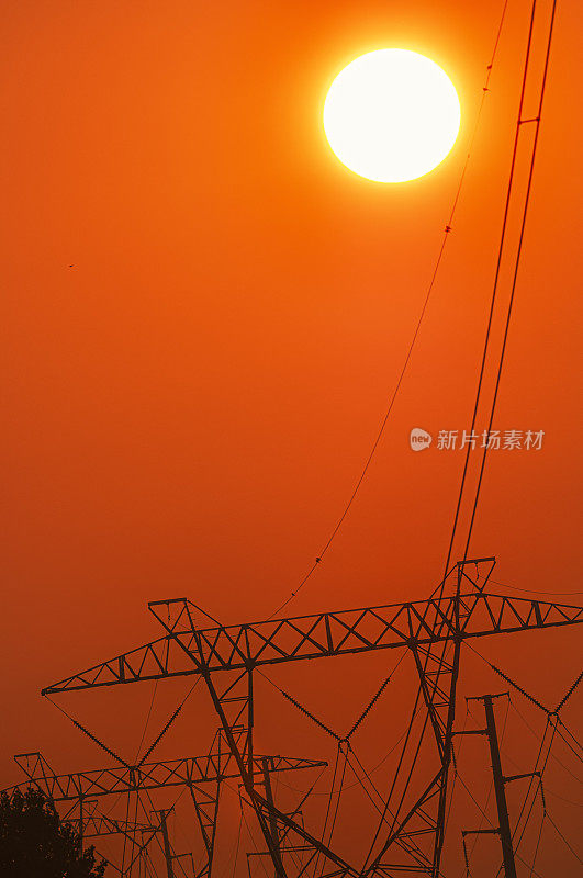 炎炎夏日，太阳落在一排高压输电塔后面