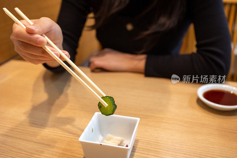 一名亚洲妇女用筷子拿起黄瓜“Tsukemono”泡菜