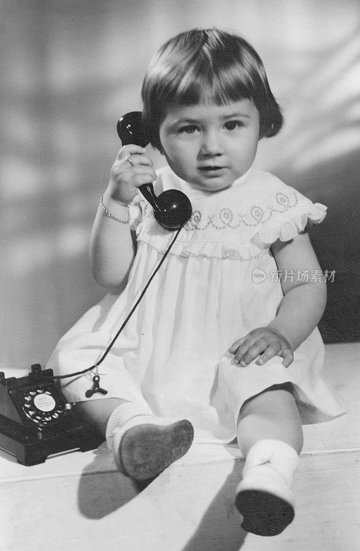 黑白照片拍摄于50年代末，小女孩摆姿势拿着手机看着相机