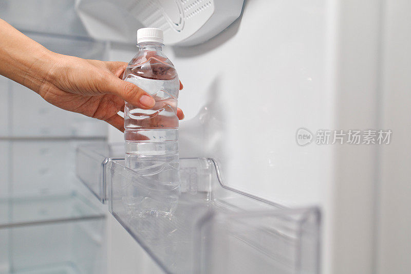 一个年轻女子从冰箱的架子上拿出一瓶水的短镜头