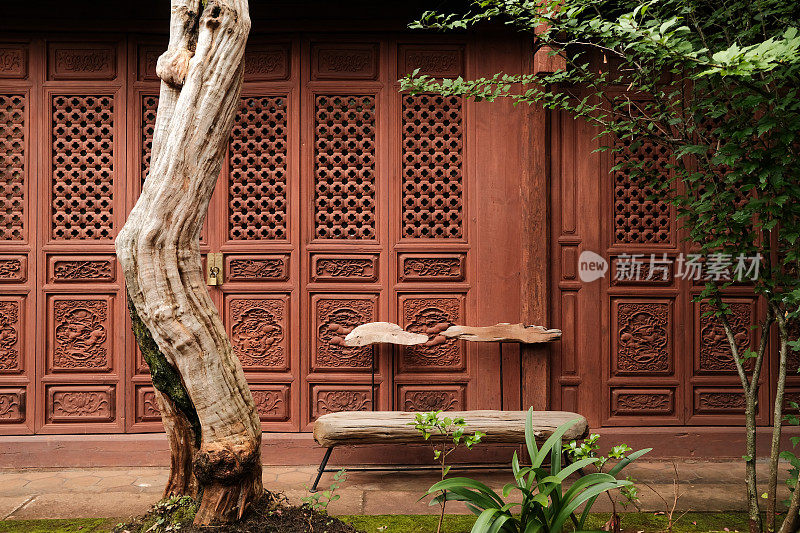 云南省的中国传统四合院。古村宅院花园，花草树木。庭院的木凳和植物立面上的中式木制屏风纹理。