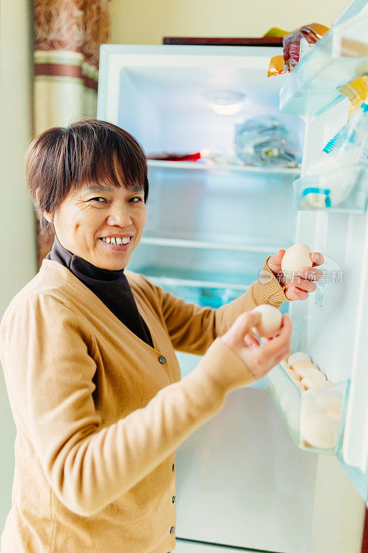 一位中年妇女从冰箱里拿出鸡蛋准备早餐——健康的生活方式，家庭生活