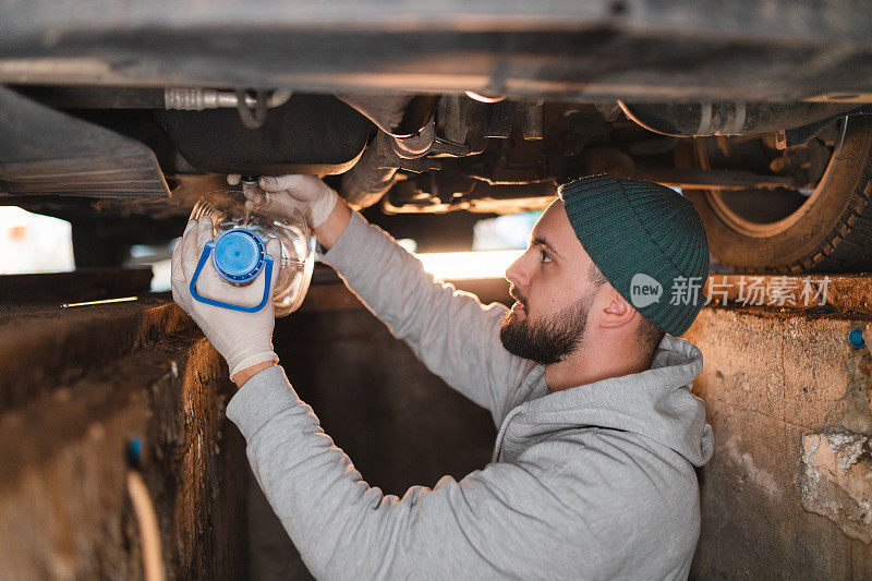 年轻的机械师在车下的运河里给车加油