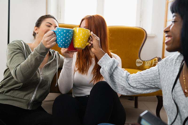 三位女性朋友拿着装有热饮的杯子欢呼。团结友爱的理念。
