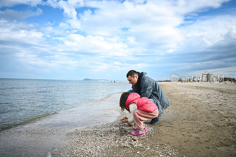 小女孩和爸爸一起捡贝壳。