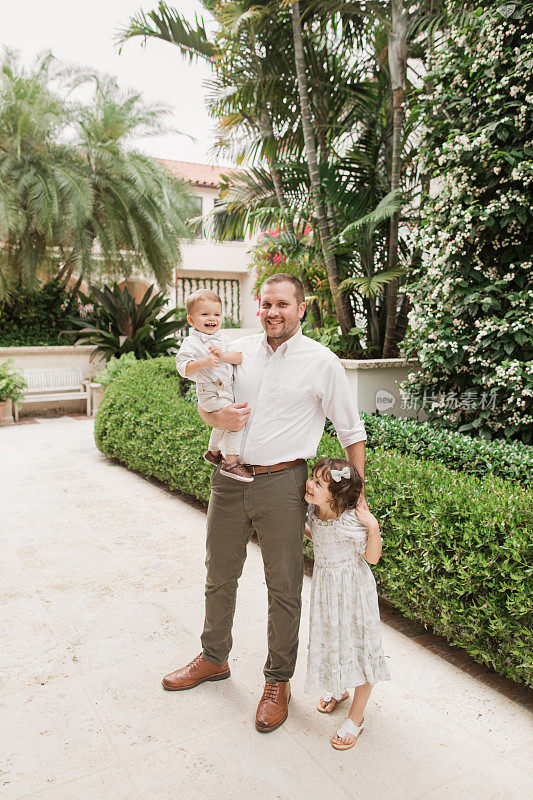 2023年5月，佛罗里达州棕榈滩，一位美国父亲与他4岁的古巴裔美国女儿和1岁的男婴的坦诚时刻，他们都是浅棕色头发，穿着鼠尾草绿和白色的春装