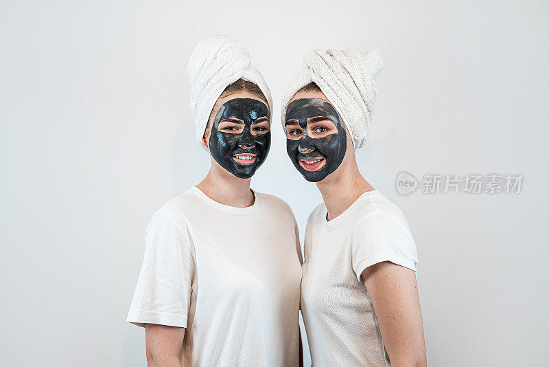 两个姐妹或女友的肖像使皮肤面膜隔离在白色上