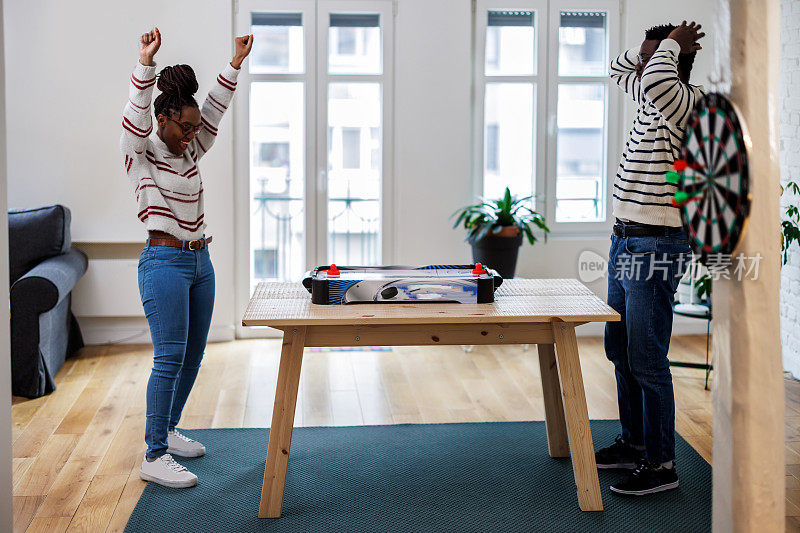 一个年轻英俊的非洲男子正在家里和他的女朋友打桌上曲棍球。