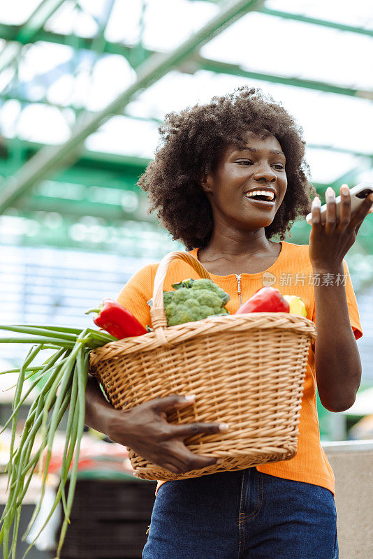 一个年轻的非裔美国女人拿着一篮子食品杂货在打电话