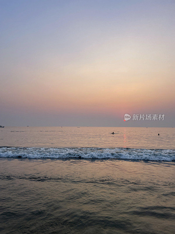 美丽的海边紫色和橙色日落的形象，日出反射在大海和潮湿的沙滩上，潮汐反射涟漪，太阳落在海滩上