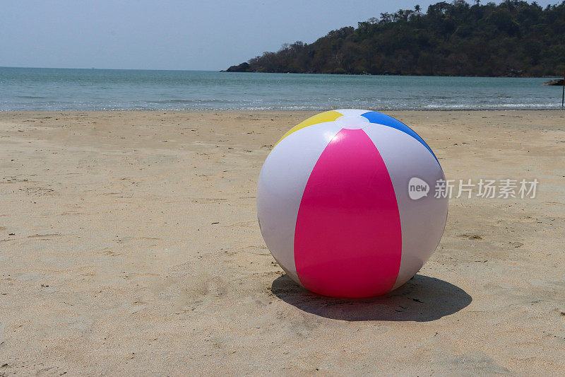 沙滩上的沙滩球特写图像，塑料，色彩鲜艳的儿童沙滩玩具，退潮时的大海，林地海岸线背景，重点在前景