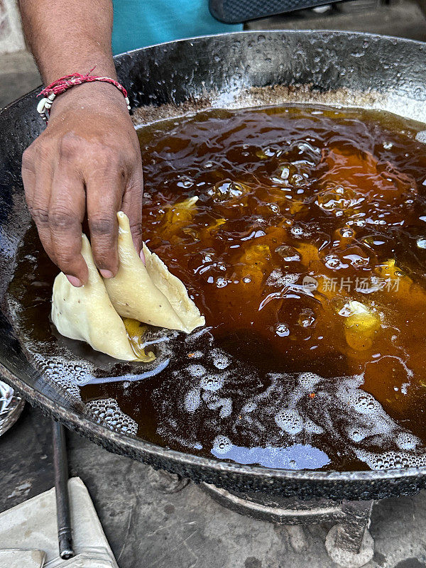 特写图片:无法辨认的人将samosas放入karahi(印度锅)，冒泡的热油，油炸的samosas，印度街头小吃摊，不健康的饮食，抬高的视角，聚焦于前景