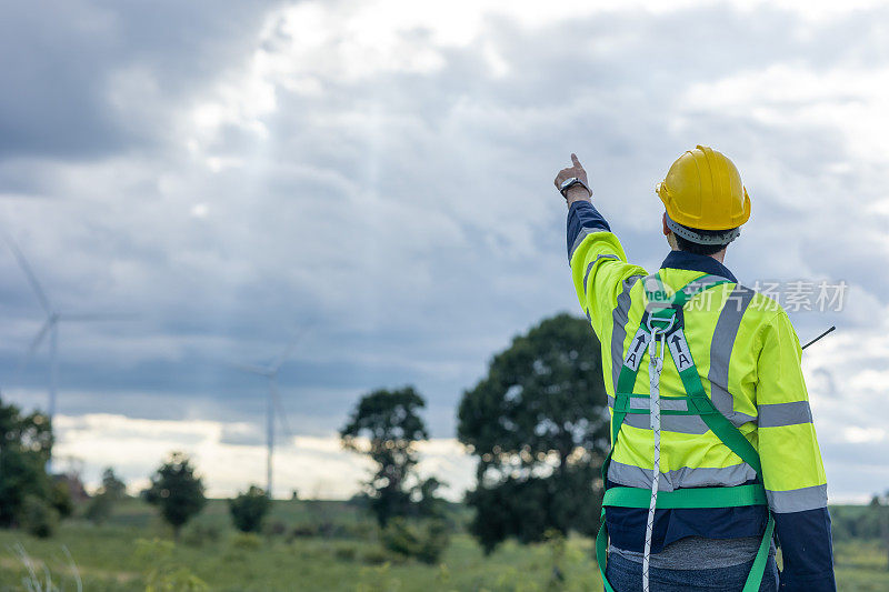 在风力涡轮机农场工作的工程师男向后看，手指着天空，为未来的生态清洁能源工人的人