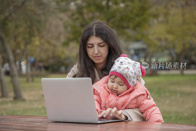 一个女人在大自然中摆弄着她的电脑，她的孩子坐在她的腿上。