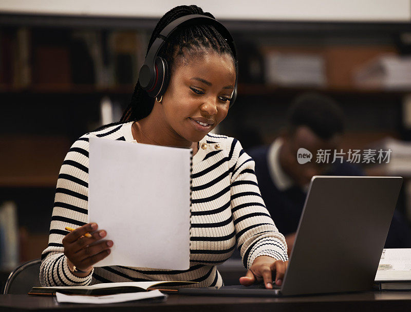 女性，在大学图书馆里学习，戴着耳机进行研究、文件和计算机研究或规划。非洲学生阅读报纸，听音乐或笔记本电脑来集中注意力和电子学习