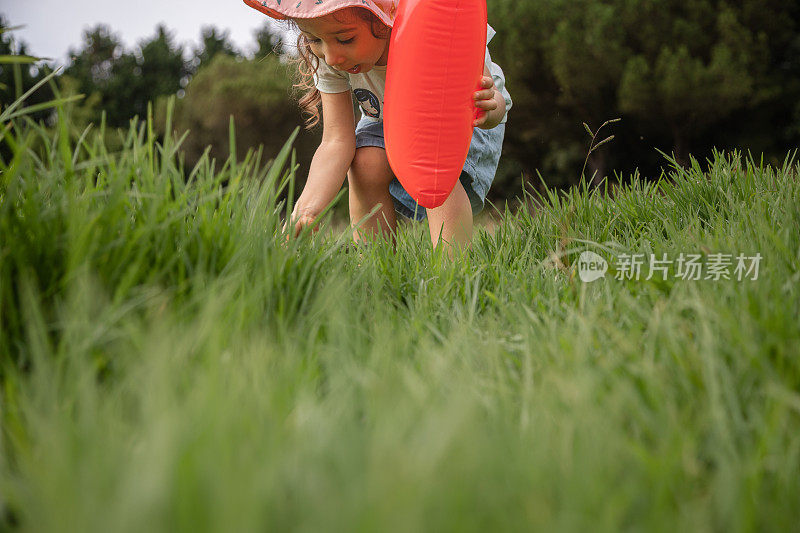 快乐童年的概念，探索你身边的世界。可爱的赤脚女孩白天在公园的草地上玩，手里拿着一个气球。
