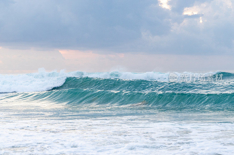 蓝绿色的海浪在多云的天空下撞击。巴厘岛，梦幻海滩。