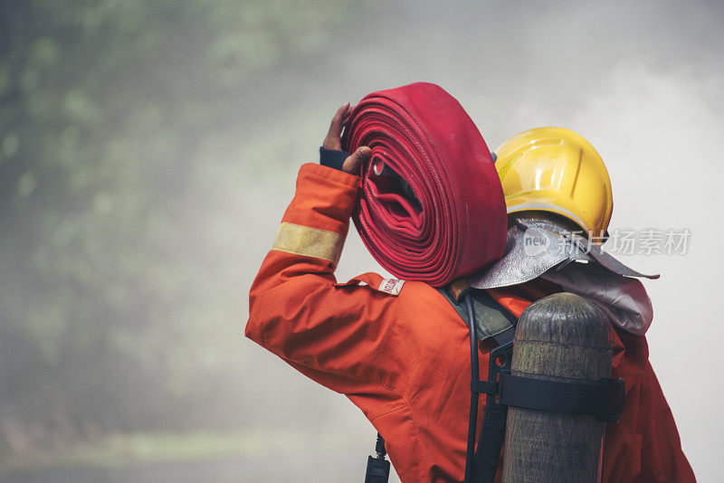 消防员灭火器救援训练。消防队员使用消防水带与火焰搏斗，化学水泡沫喷雾机。消防队员戴安全帽，穿安全防护服