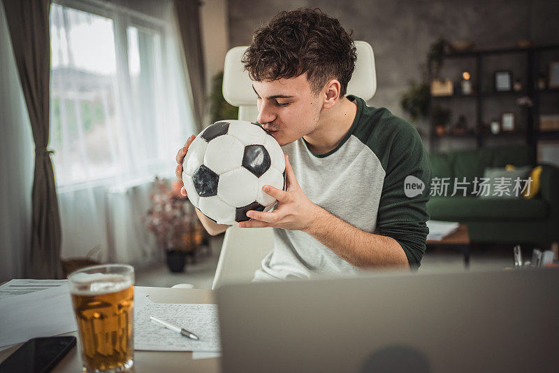 一个十几岁的孩子在课间休息，坐在书桌前用笔记本电脑看足球比赛