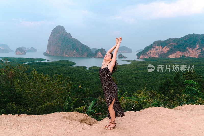 一名女子高举手臂站在攀牙湾的背景上