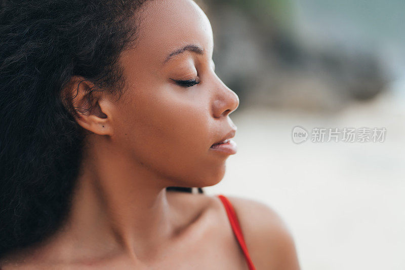 美丽的黑皮肤女孩的肖像闭着眼睛在海滩摆姿势。性感的非洲裔美国模特与卷发
