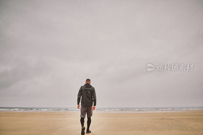 一名男子在雨中站在阴沉沉的海滩上晨跑。