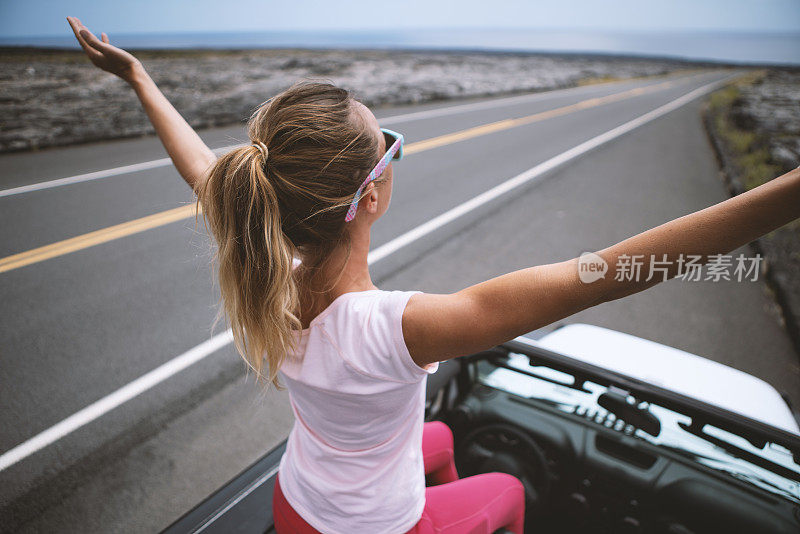 年轻女子坐在4x4汽车上，双臂伸开享受公路旅行